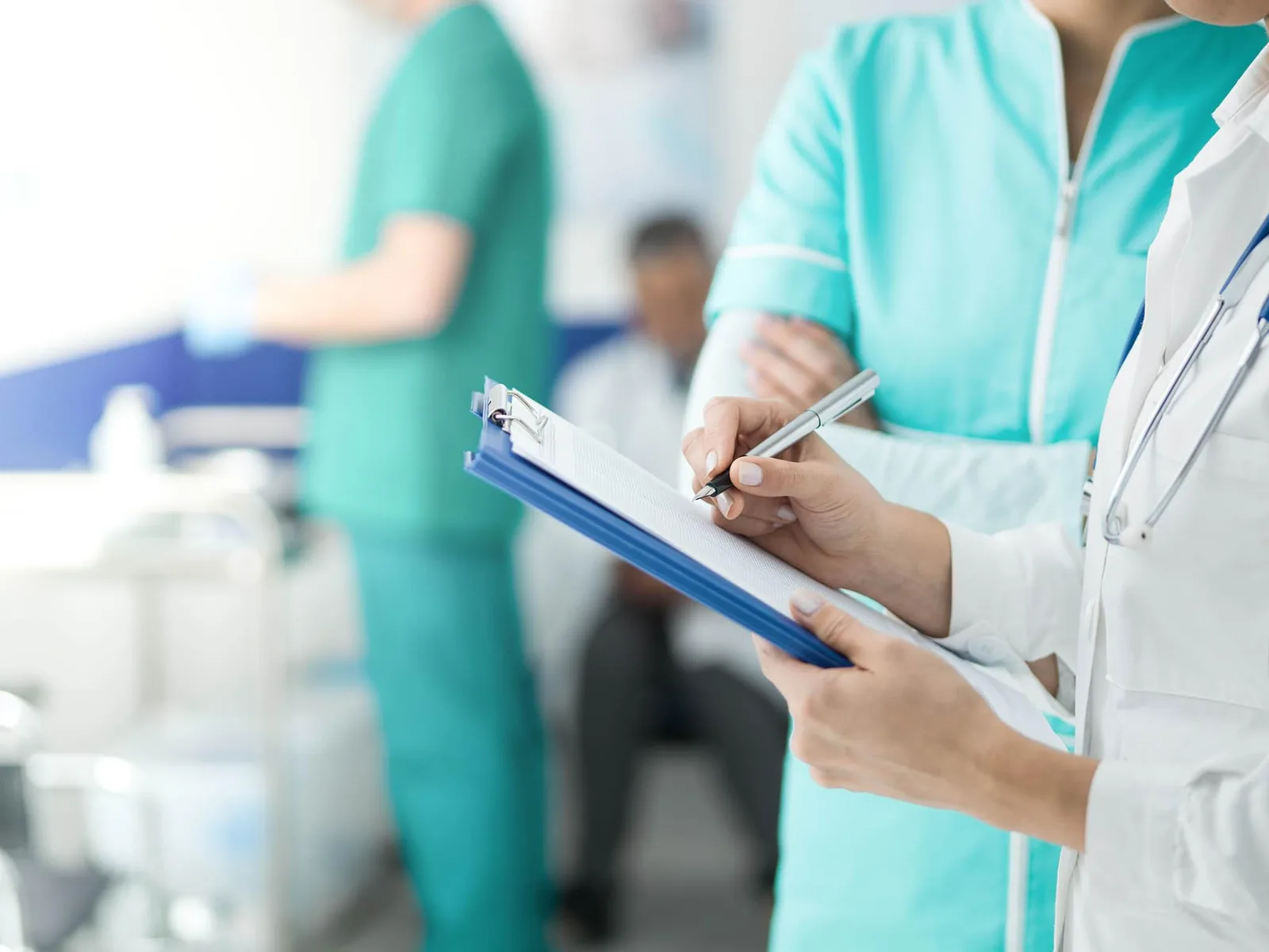 Clinical staff on a hospital ward, one writing on a clipboard